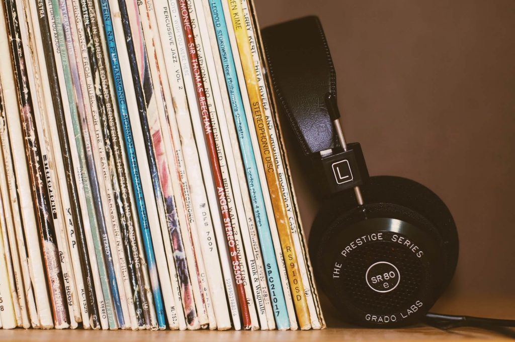 Array of vinyl records displayed on a shelf, accompanied by headphones resting nearby.